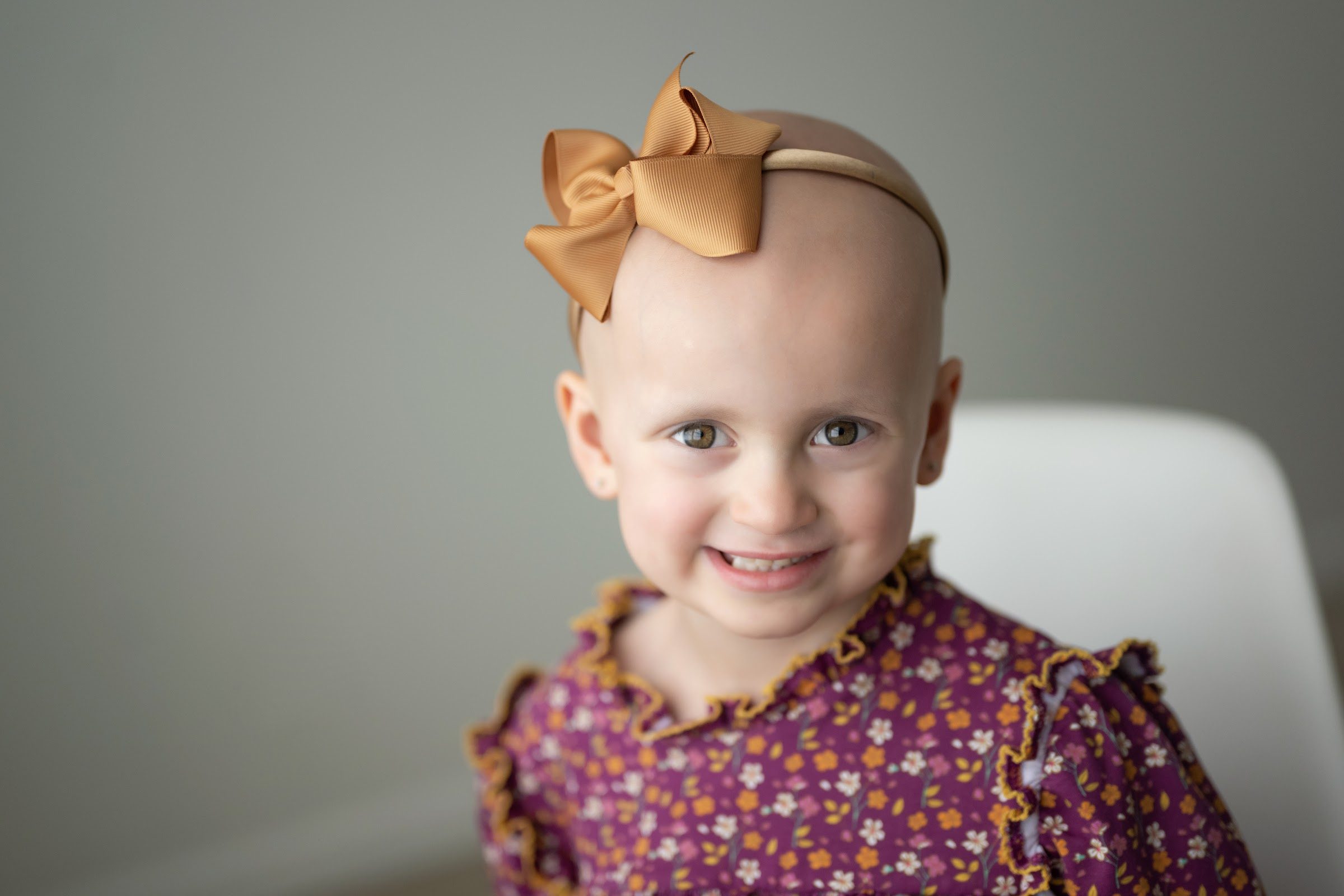 Hailey Holder, a Rally Kid, smiling in a purple floral dress and gold bow headband