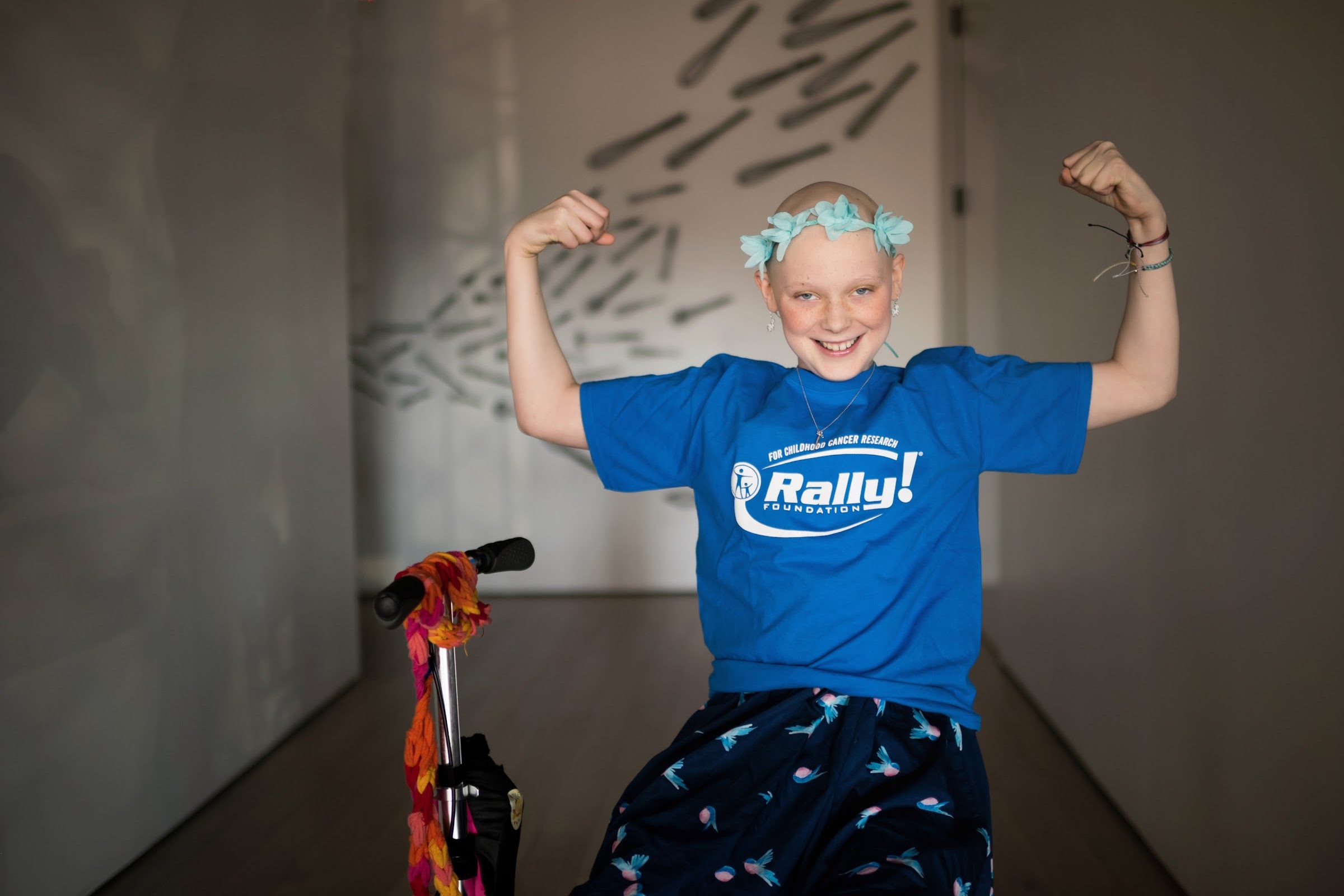 Keren, a Rally Kid, flexing both arms and smiling in a blue Rally Foundation T-shirt