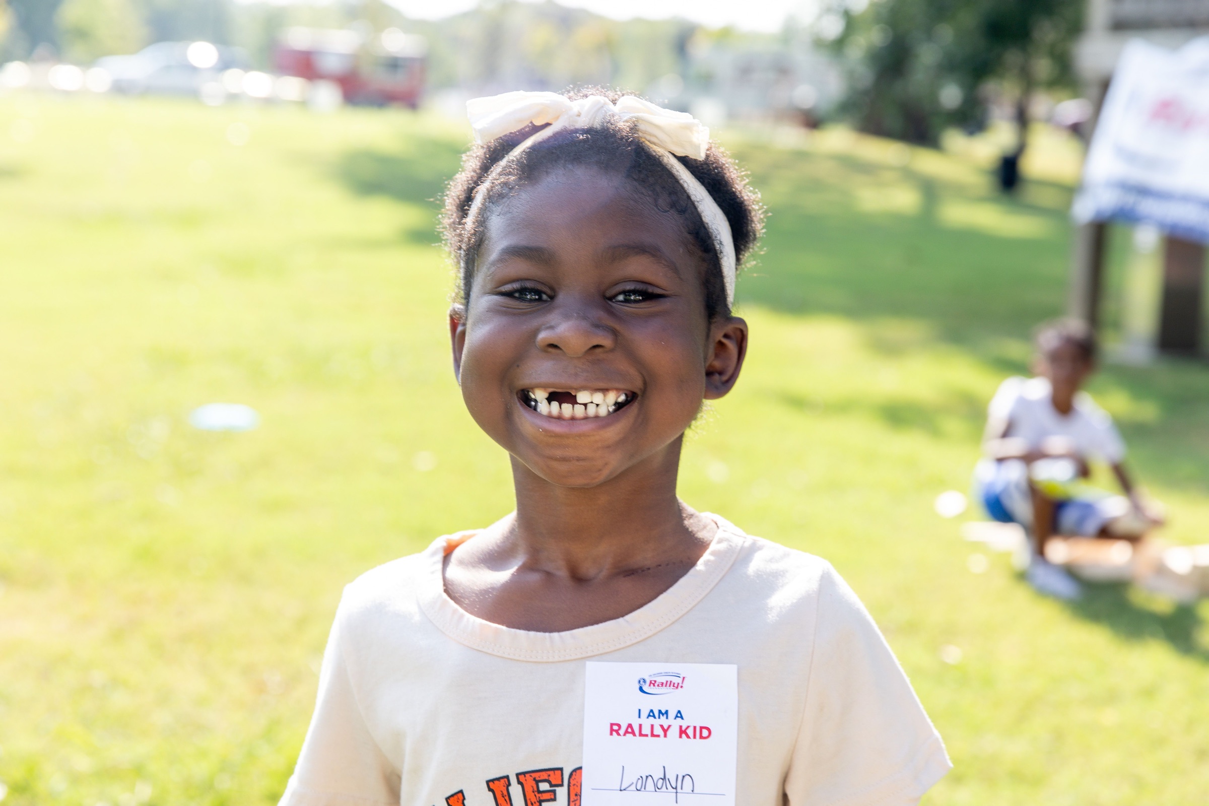 Londyn, a Rally Kid, smiling outdoors and wearing an “I am a Rally Kid” name tag